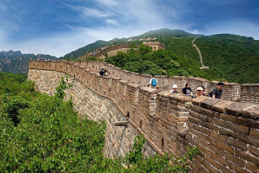 The Great Wall of China winding through lush green hills, with tourists walking along the path. 3