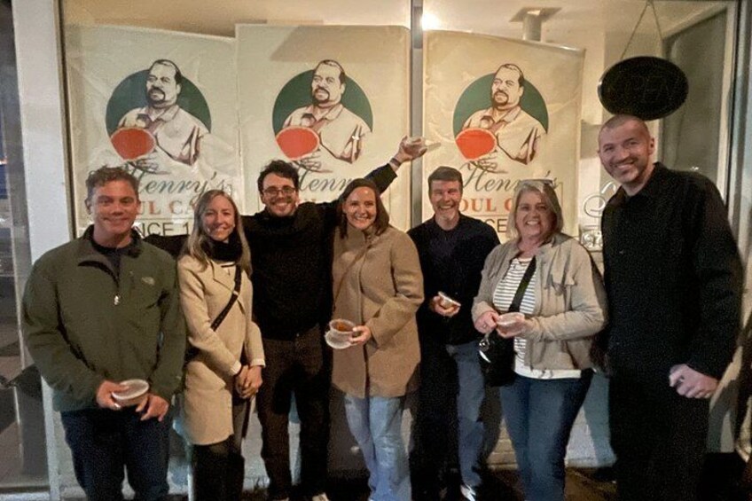 A group of people standing in front of a wall with posters, holding plates of food. 5