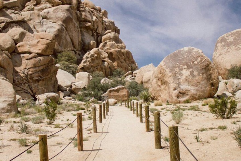 A sandy trail with wooden posts, surrounded by large boulders and sparse vegetation. 3