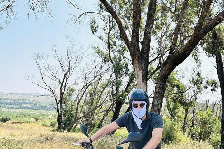 A person on a motorcycle in a natural setting with trees and a distant landscape. 4