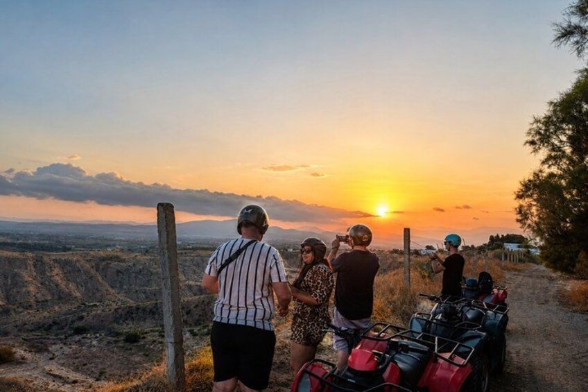 A sunset with a group of people and ATVs on a dirt path. 4