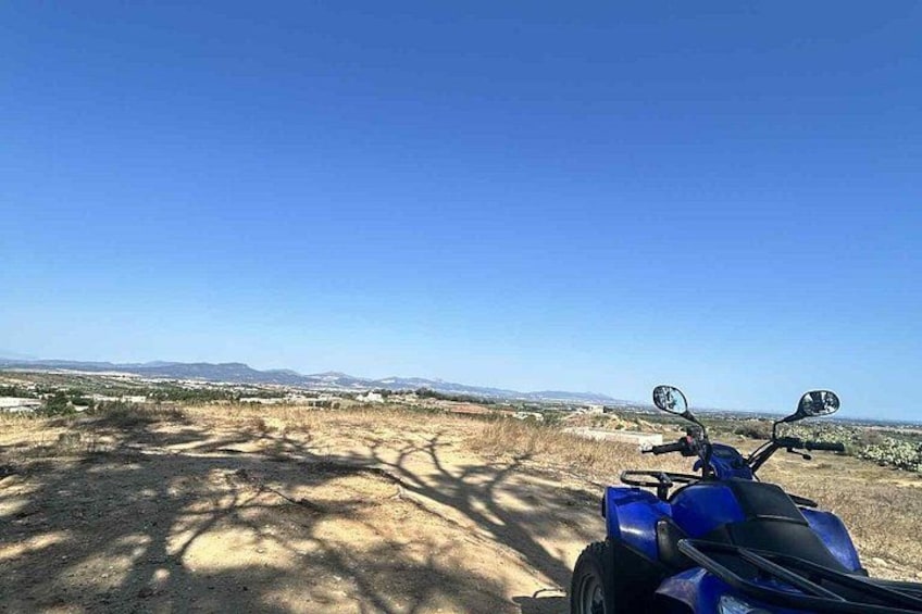 A blue ATV parked on a dirt road with a clear blue sky and distant mountains. 3