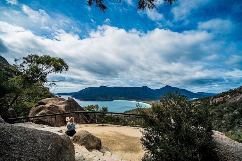 A person sitting on a rock overlooking a coastal landscape with mountains and a clear sky. 4