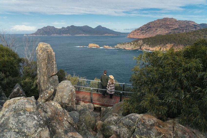 A coastal landscape with rocky outcrops, a person on a wooden platform, and distant mountains. 2
