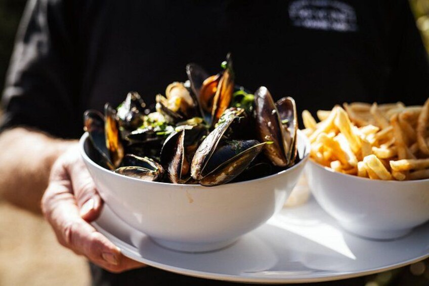 A person holding a tray with a bowl of mussels and a bowl of fries. 4