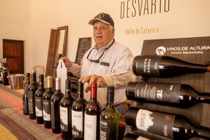 A man standing behind a table with various wine bottles. 4
