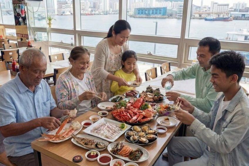 A group of people dining at a table with seafood dishes, a view of a river, and a cityscape in the background. 2
