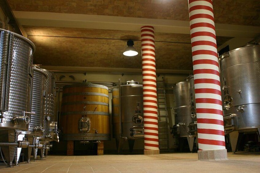 A brewery with stainless steel tanks and wooden barrels, red and white striped columns, and a brick ceiling. 1