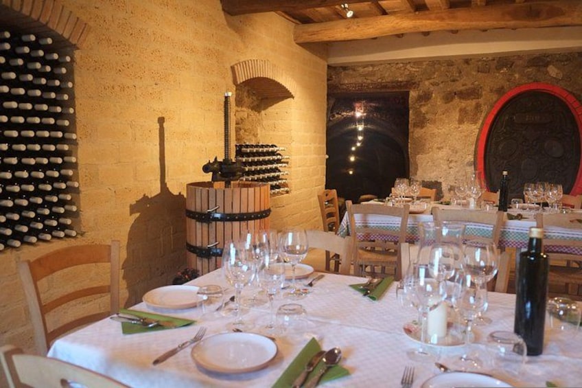 A dining table set with plates, cutlery, and wine glasses, surrounded by stone walls and wine racks. 2