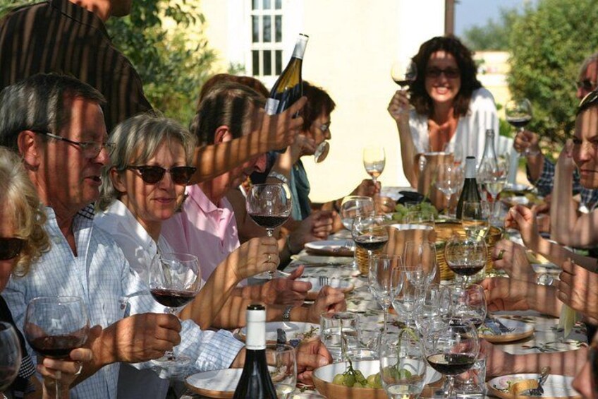 A group of people seated around a table with wine glasses and bottles, outdoors. 4