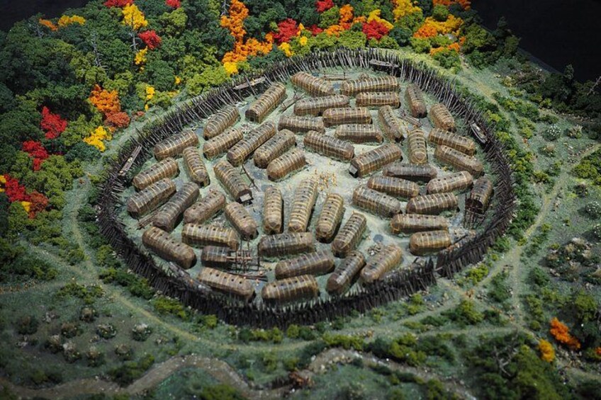 A circular arrangement of cylindrical structures surrounded by a fence, with a forested area in the background. 4