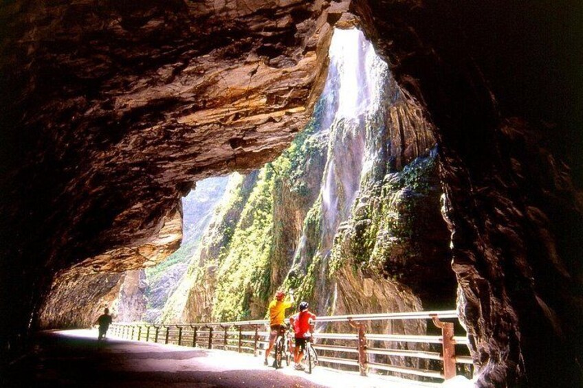 Eine Höhle mit einem Wasserfall, einem gepflasterten Weg und einem Geländer. 4