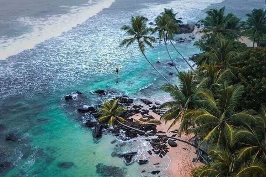 A beach with clear turquoise water, palm trees, and rocky outcrops. 2