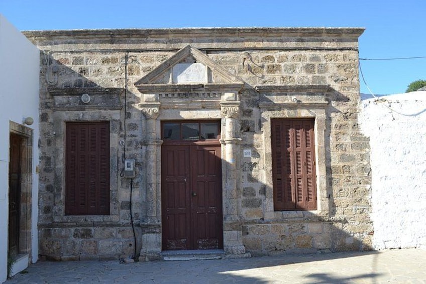A stone building with a central door and two windows, each with wooden shutters. 4