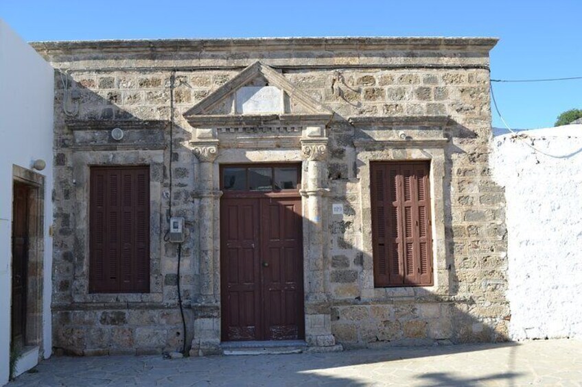 A stone building with a central door, flanked by two windows with shutters. 4