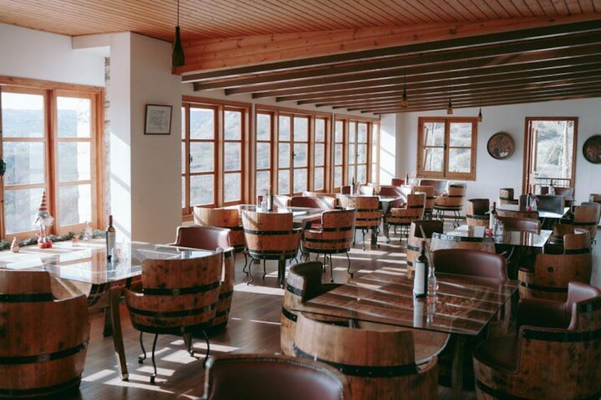 Un interior rústico con barriles de madera utilizados como mesas y sillas, ventanas amplias y techo de madera. 2