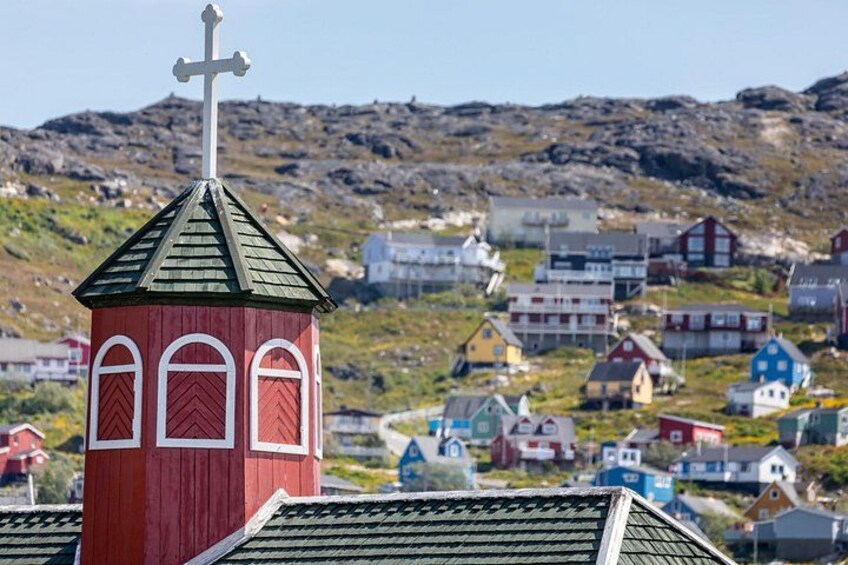 A red church with a cross on top, surrounded by colorful houses in a hilly village. 1