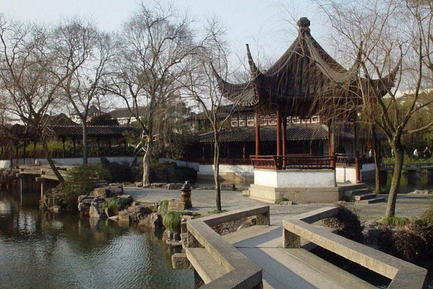 A traditional pavilion by a tranquil pond, surrounded by bare trees and stone steps. 2