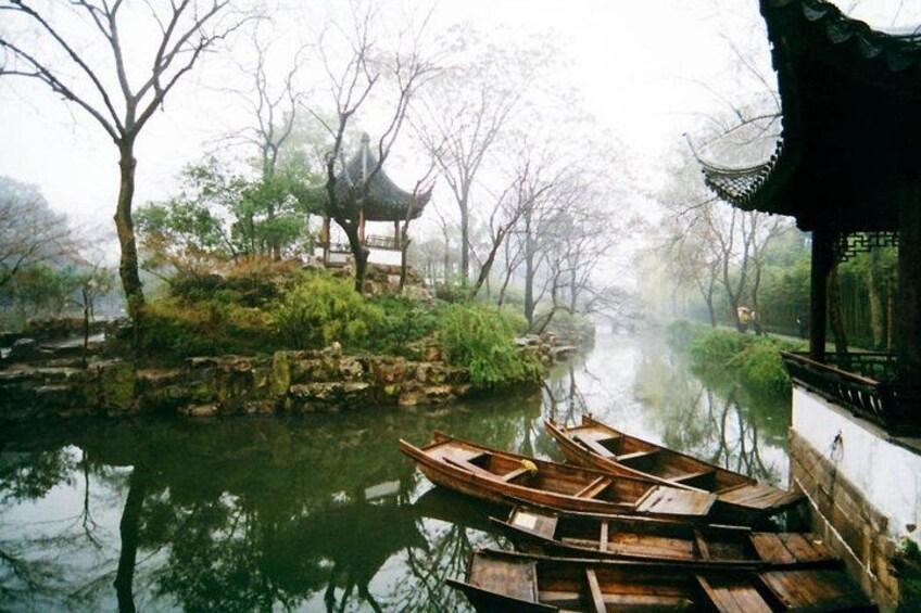 A serene riverside scene with traditional wooden boats docked, a stone bridge, and a pavilion. 3