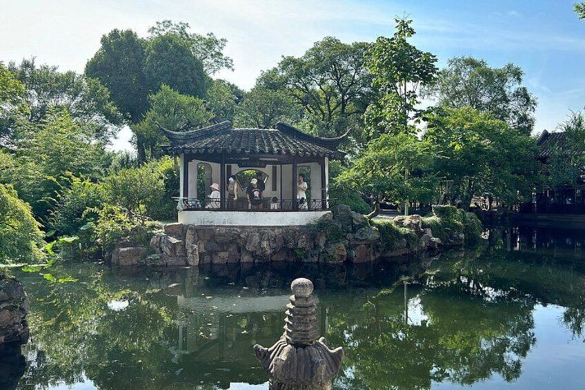 A traditional pavilion by a pond with a statue in the foreground. 1