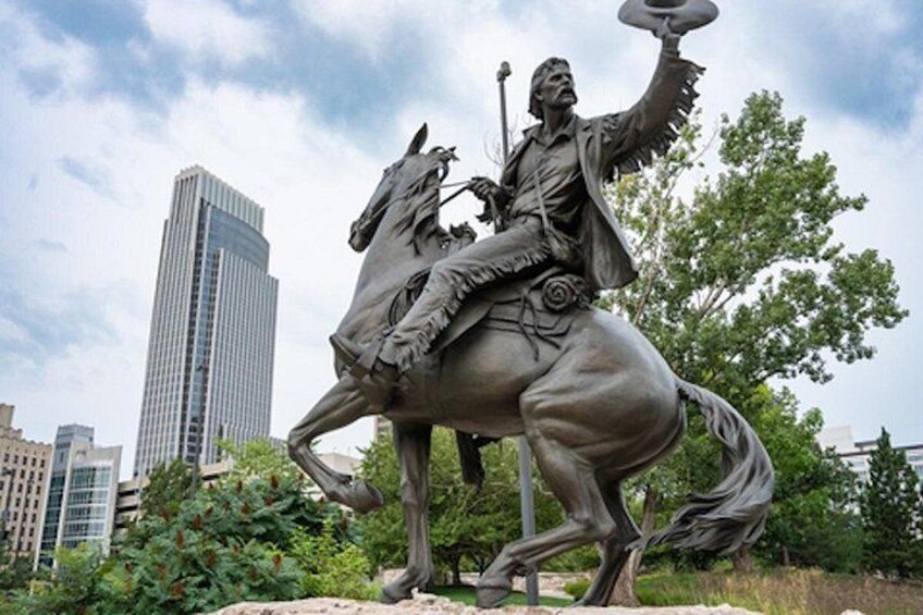 A statue of a man on horseback with a raised arm, set against a cityscape with modern buildings and greenery. 1