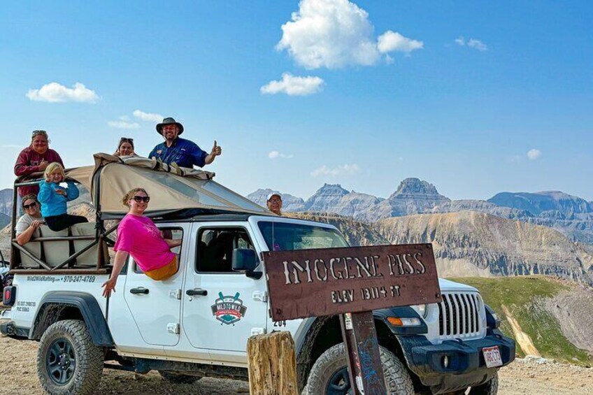 A white off-road vehicle with a sign reading "HIGGEE PASS" and a group of people on top. 5