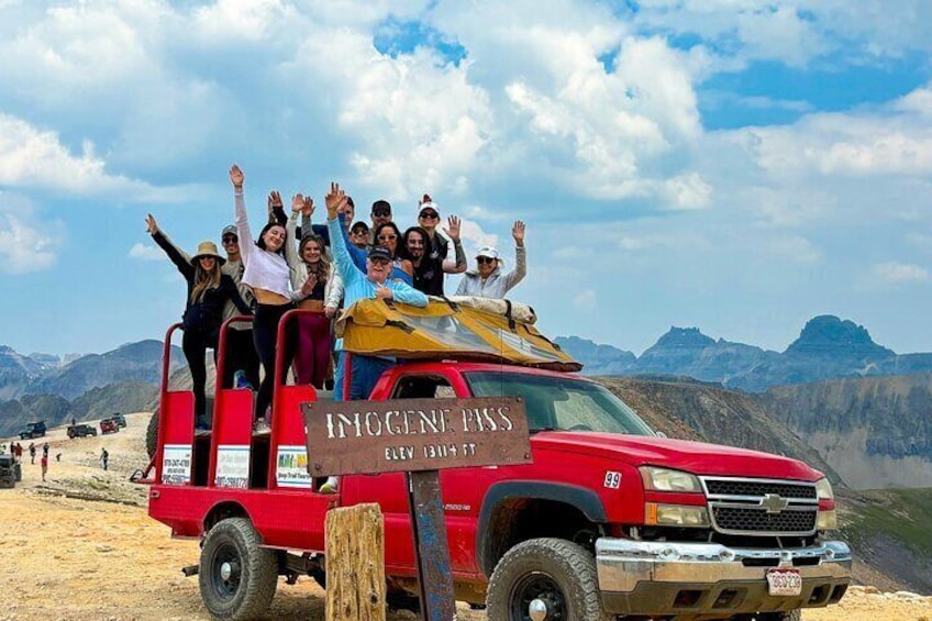 A group of people on a red truck with a sign reading "Imogene Pass" and "Elevation 13100 ft." 1