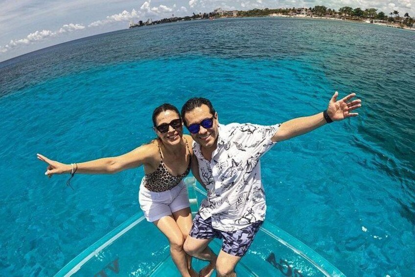 Two people on a boat in clear blue water with a beach and buildings in the background. 2