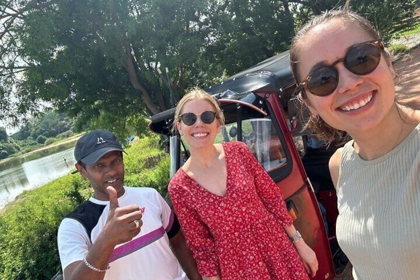 Three people standing by a river with a vehicle in the background. 1