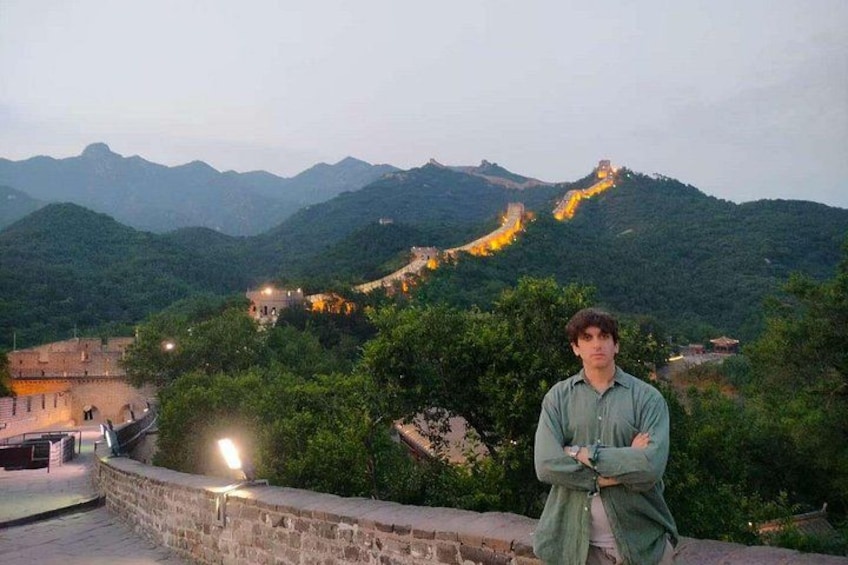 A person standing on a stone wall overlooking a mountainous landscape with a brightly lit path. 2