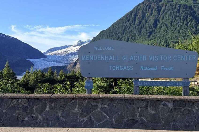 En välkomstskylt vid besökscentret för Mendenhallglaciären, med glaciären synlig i bakgrunden. 4
