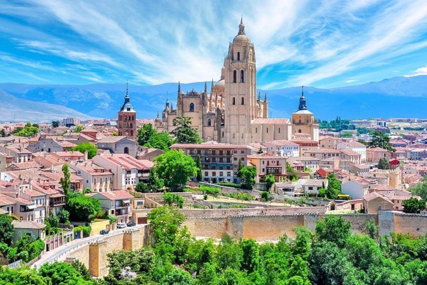 A historic cityscape with a prominent cathedral, lush greenery, and a mountainous backdrop. 1