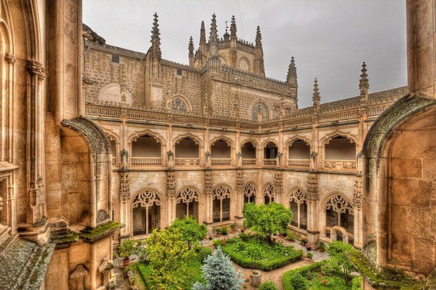 Un claustro histórico con intrincados trabajos en piedra, un patio central y un edificio grande con múltiples agujas. 3