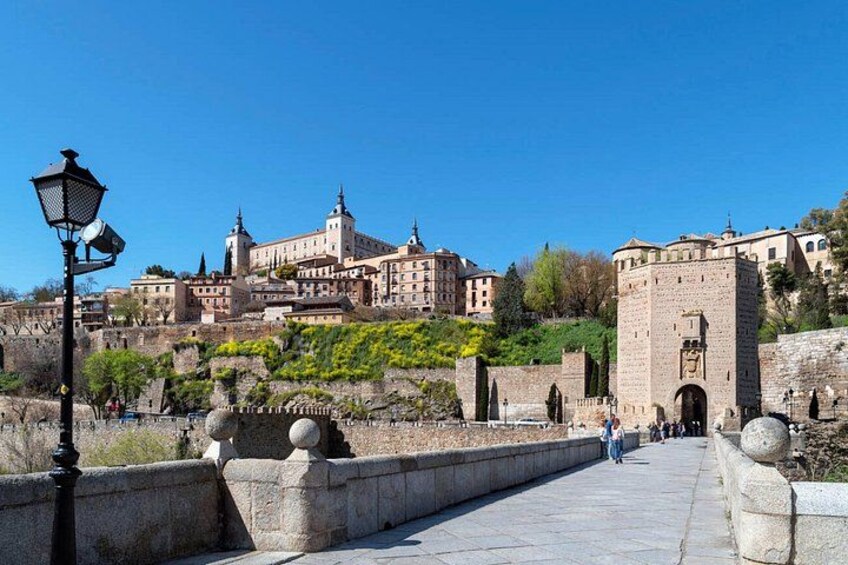 Un puente de piedra con un farol, un castillo al fondo y un cielo azul despejado. 4