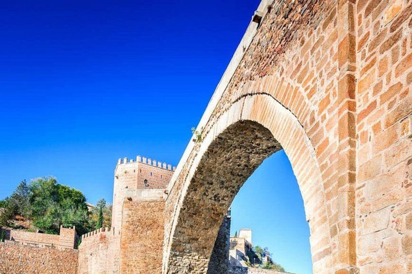 A stone bridge with an arch, a castle in the background, and a clear blue sky. 2