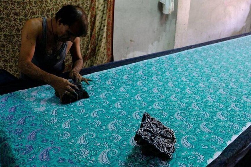 Une personne est assise sur un lit recouvert d’une couvre-lit à motifs et tient un objet sombre dans ses mains. 2