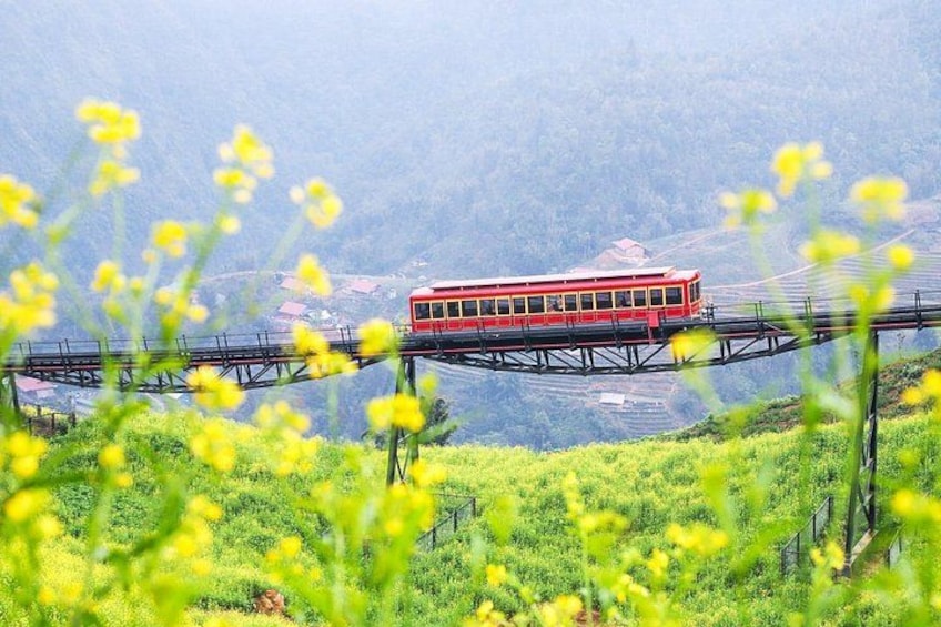 A red train on a bridge over a river, surrounded by greenery and mountains. 2