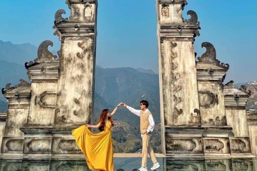 A couple holding hands in front of an ornate stone gate with mountains in the background. 4