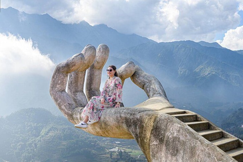 A person sitting on a large hand sculpture with a mountainous landscape in the background. 5