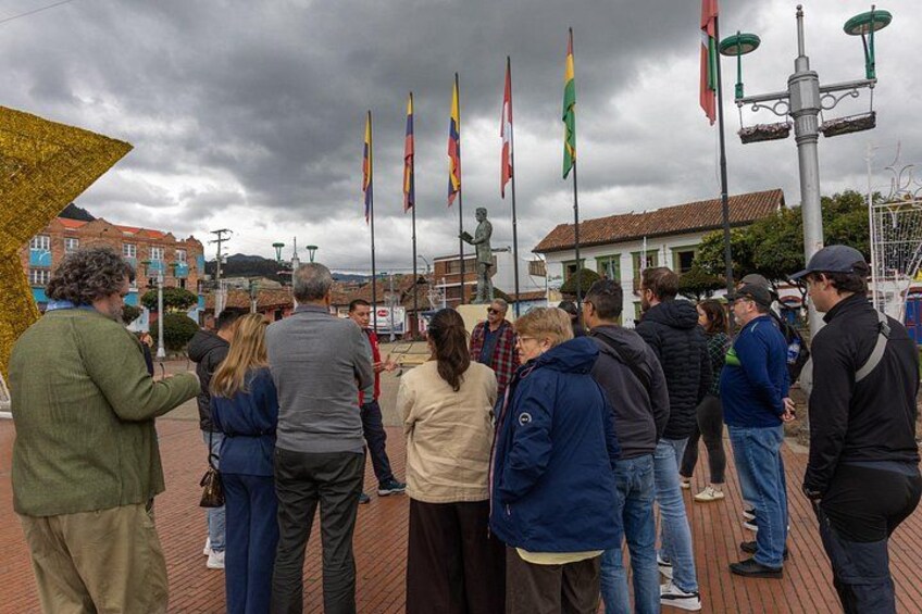 A group of people standing outdoors, a statue, and multiple flags. 4