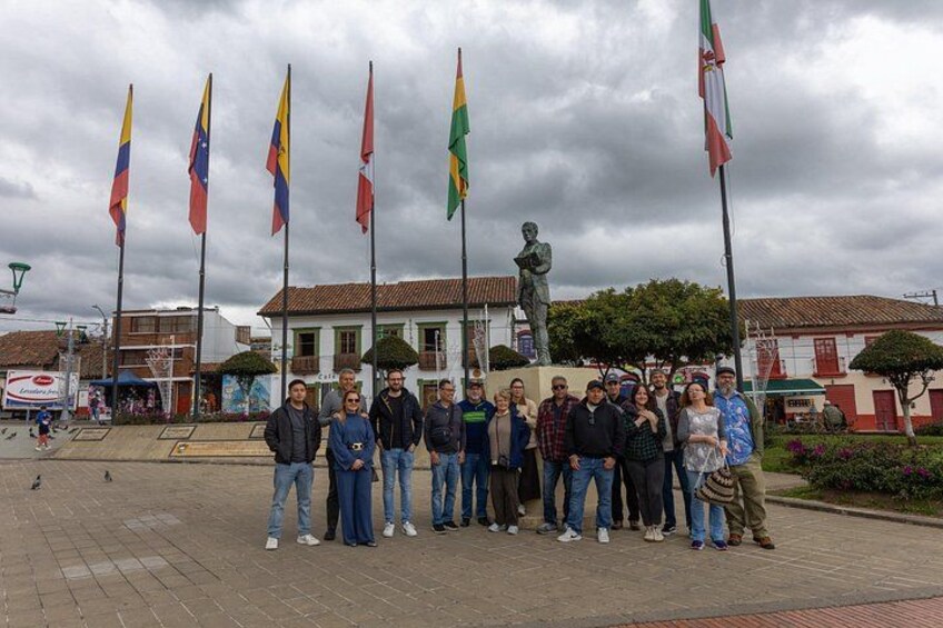 A group of people standing in front of a statue with multiple flags in the background. 5