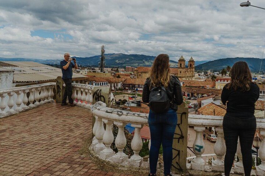 A group of people on a bridge overlooking a city with historical buildings and mountains in the background. 2