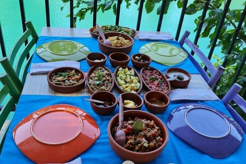 A table set with various dishes and bowls, surrounded by chairs, on a terrace with a view of water. 3