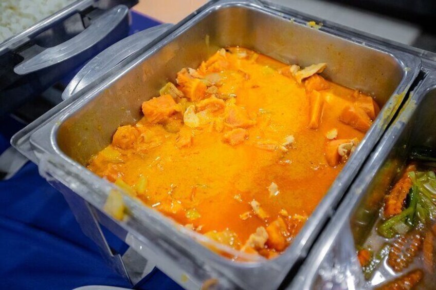 A buffet with a variety of dishes, including a prominent orange curry and other mixed dishes in metal containers. 4