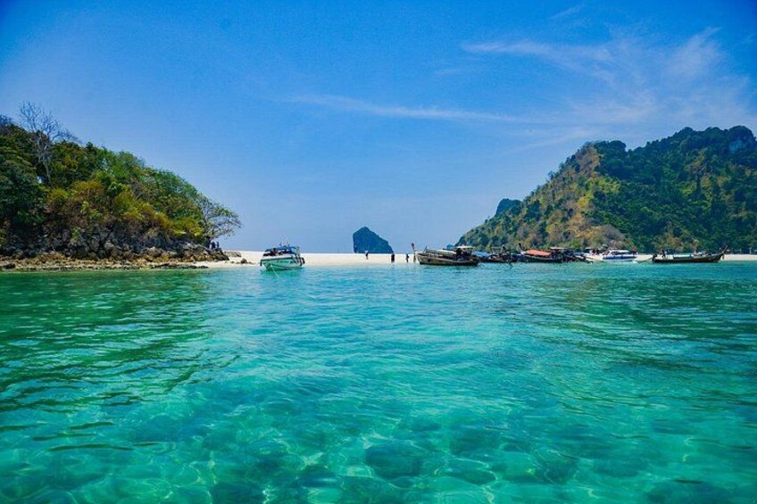 A clear turquoise sea, boats, a small hut, and a mountainous landscape. 1
