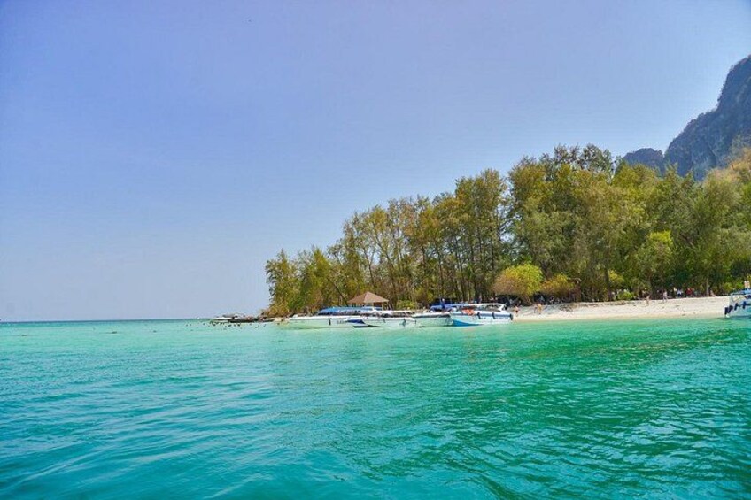 A beach with clear turquoise water, boats, and a forested hill in the background. 2