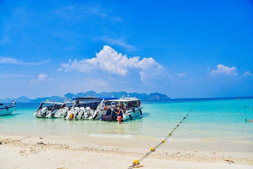 A beach with a boat docked near the shore, clear turquoise water, and distant islands. 5