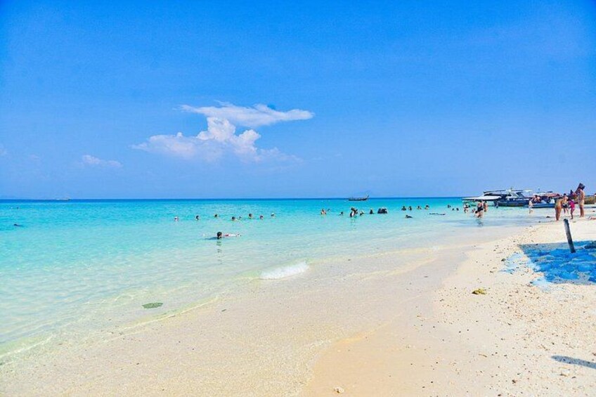 A beach with clear turquoise water, people swimming, and boats in the distance. 4