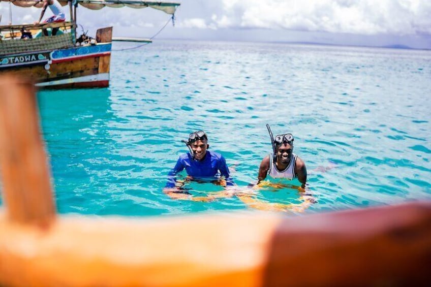 Dos personas haciendo snorkel en aguas azules cristalinas, con un barco al fondo. 2