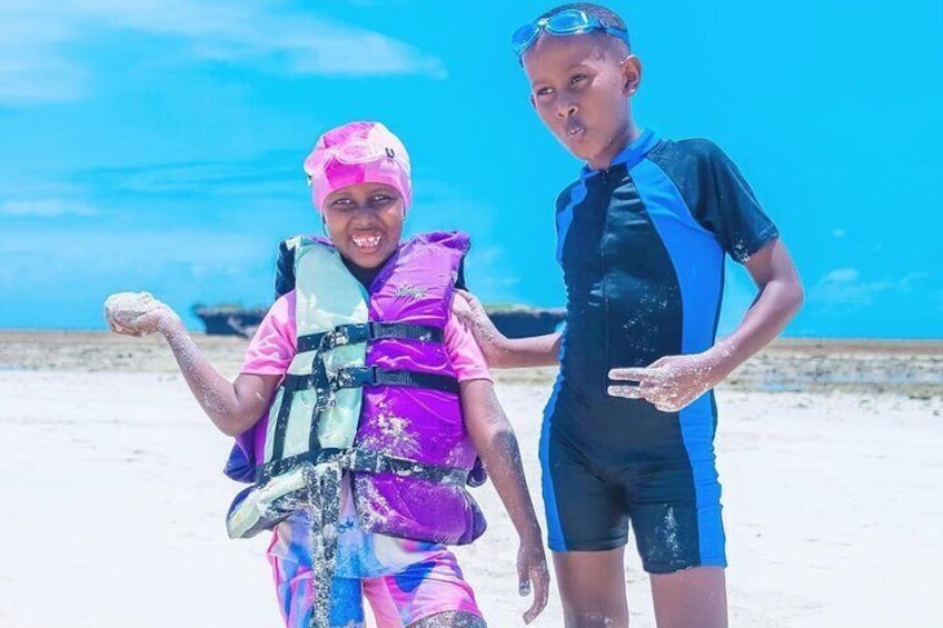 Dos personas en la playa, una usando un chaleco salvavidas rosa y la otra un traje de neopreno azul y negro. 4